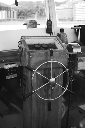 A vintage-looking ship's helm station with a wooden steering wheel and gauges. The interior has a rustic feel and includes communication equipment like a radio.