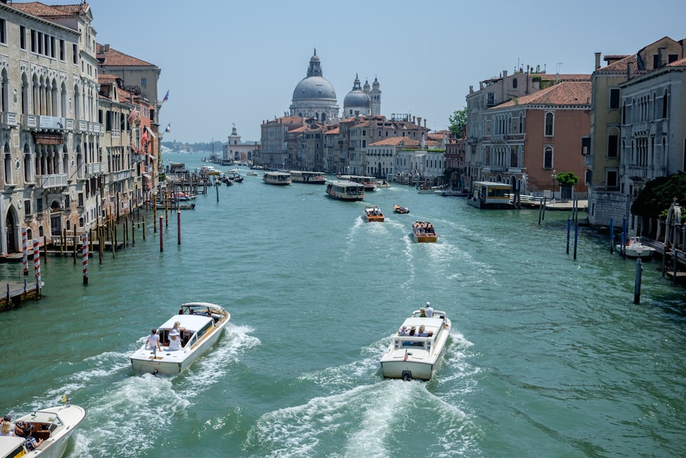 a group of boats traveling down a river next to tall buildings