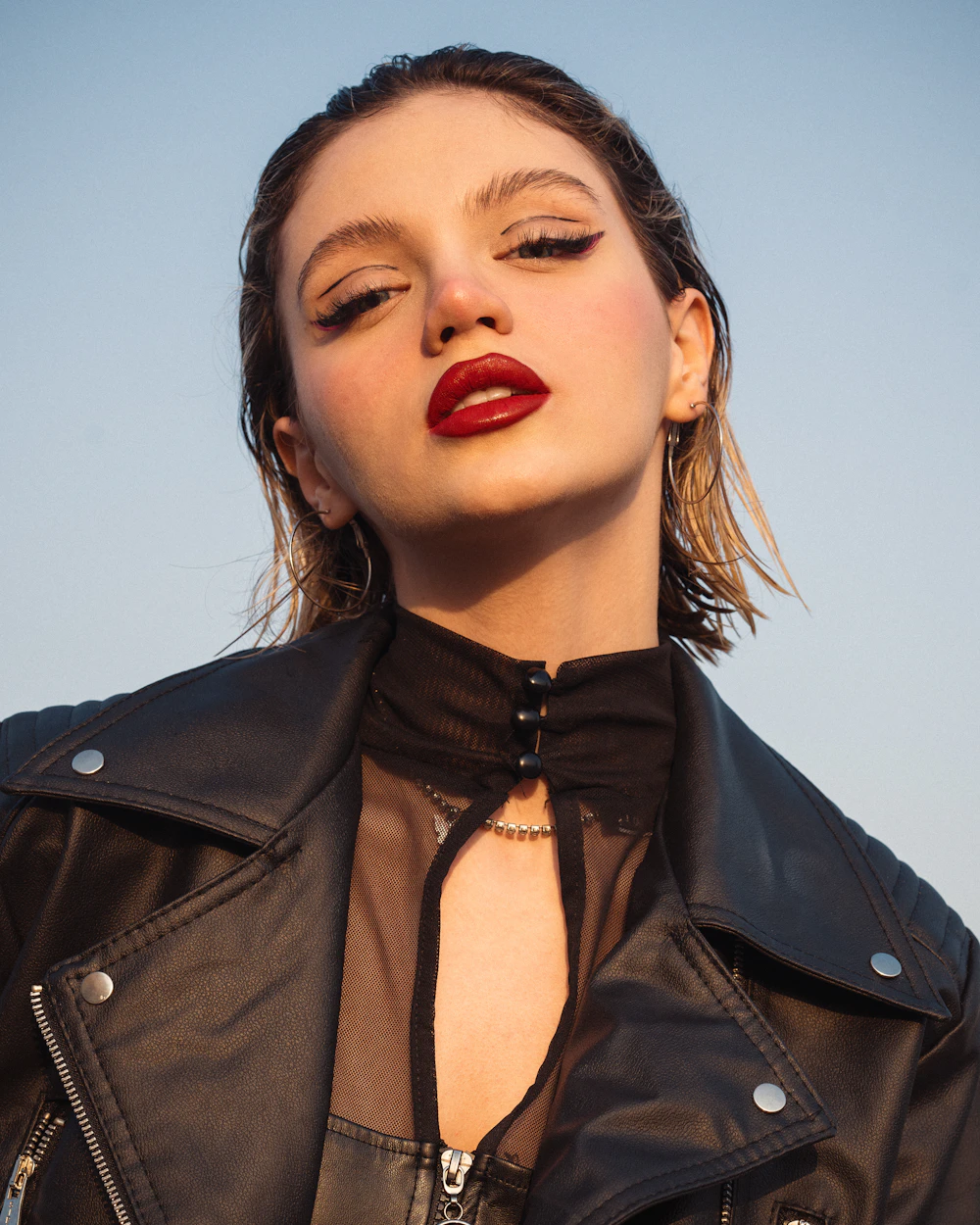 Margaux against a pale evening sky in a leather jacket, looking down at the camera.