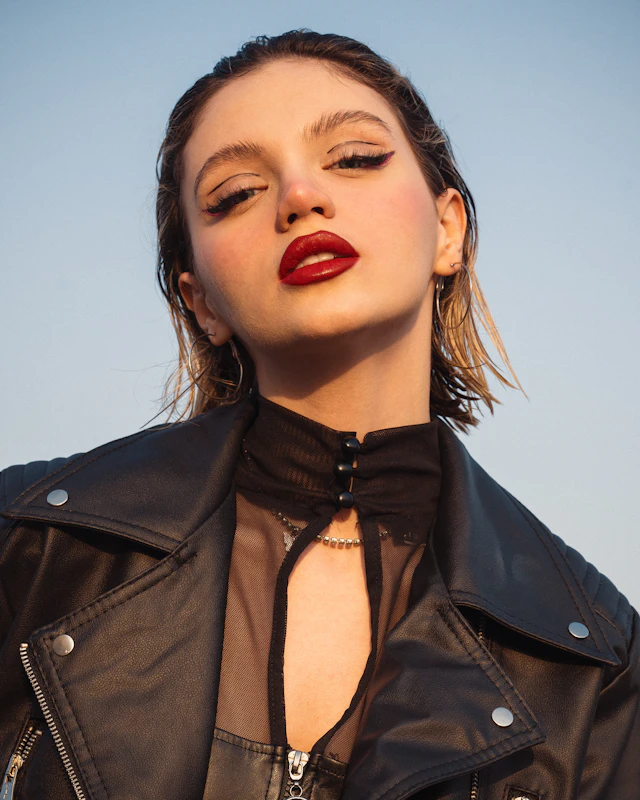 Margaux against a pale evening sky in a leather jacket, looking down at the camera.