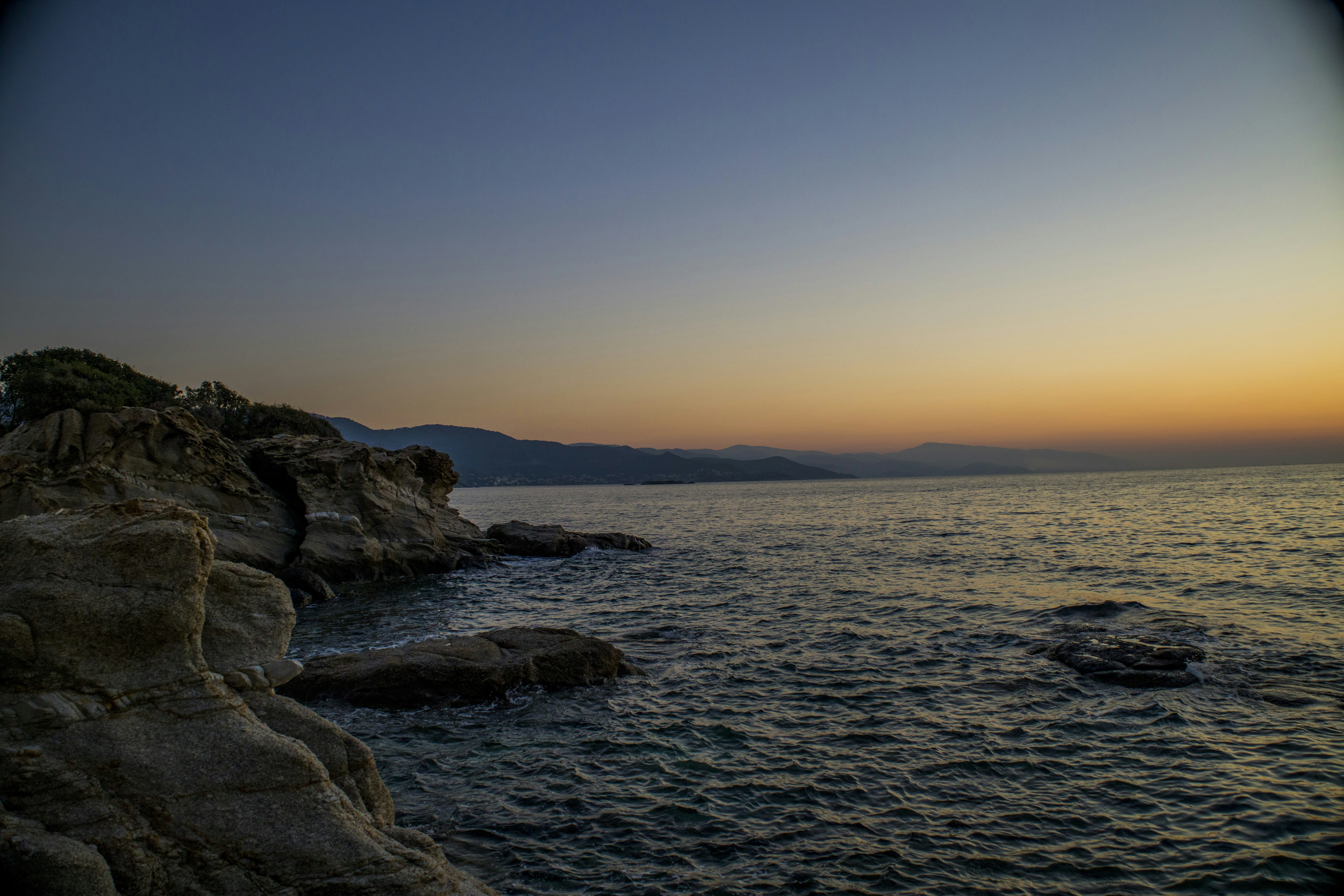the sun is setting over the ocean with a rock outcropping