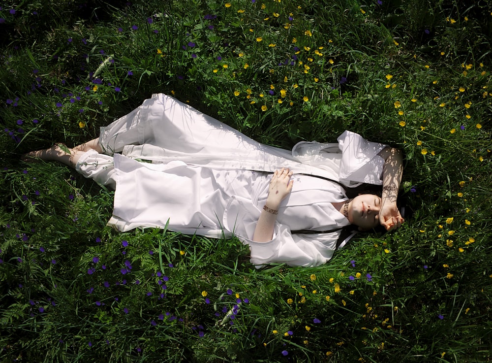 a woman in a white dress laying in a field of flowers