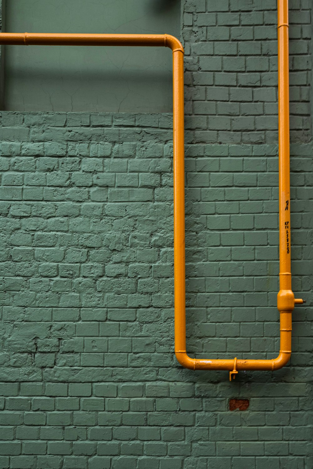 an orange pipe on a green brick wall