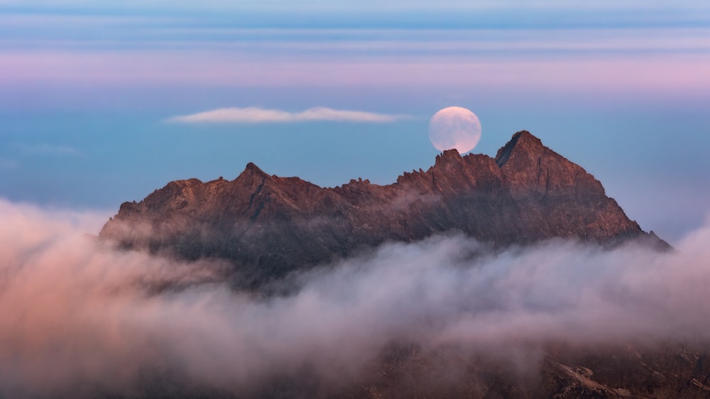a full moon is seen above the clouds on top of a mountain