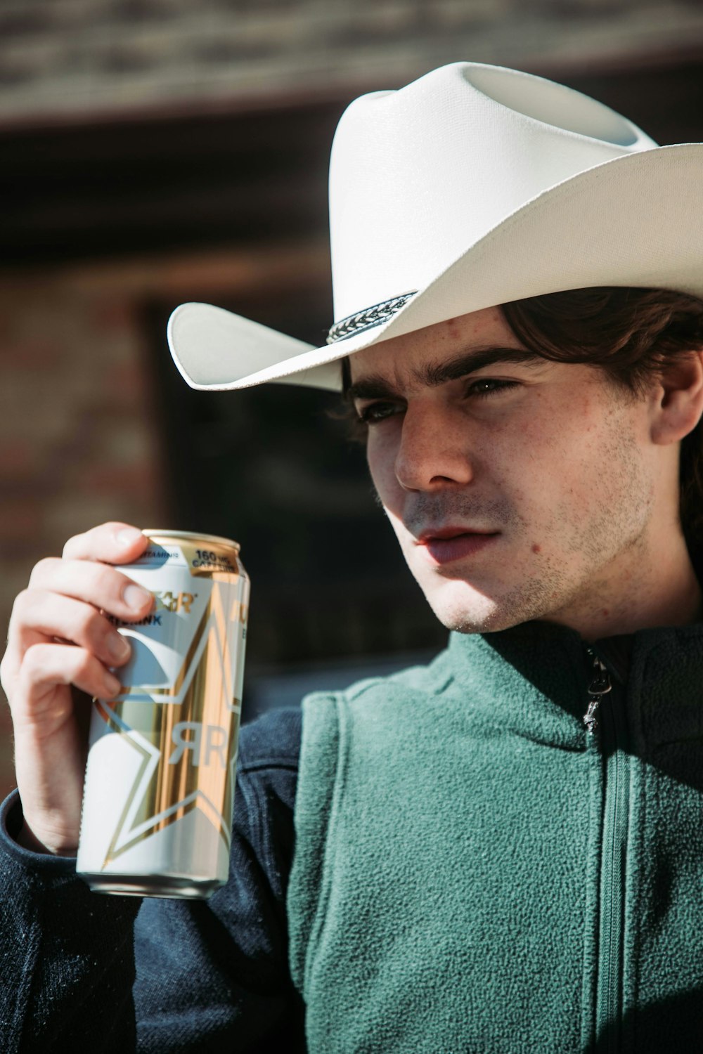 a man in a cowboy hat holding a can of beer