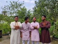 A group of men dressed in coordinated kurta sets in warm beige and maroon tones, celebrating a festive occasion.