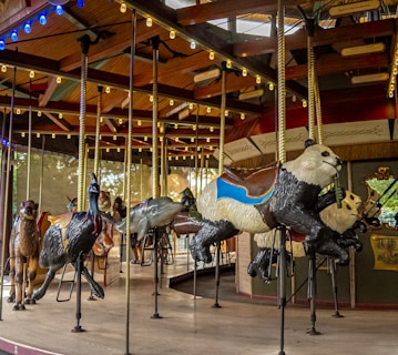 A vintage carousel with various animal figures such as a panda, dolphin, and camel. The animals are detailed and brightly painted, and the carousel is under a roof with colorful lights.