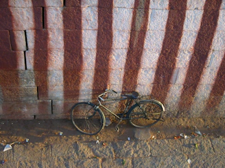 An old, rusty bicycle leaning against a weathered brick wall.