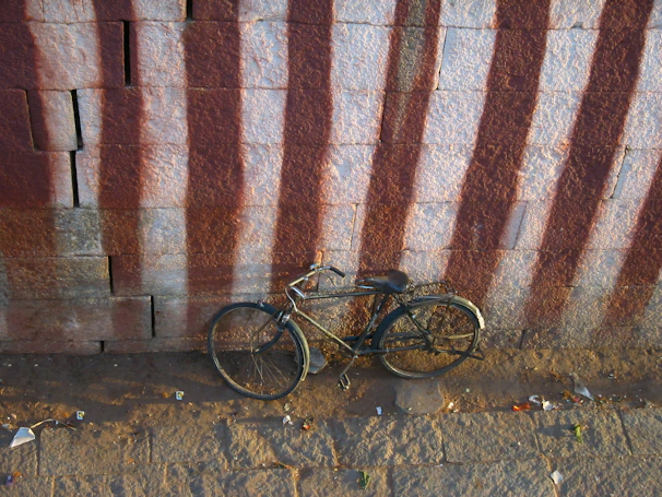 An old, rusty bicycle leaning against a weathered brick wall.