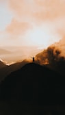 A woman standing confidently on a mountain peak at sunrise.
