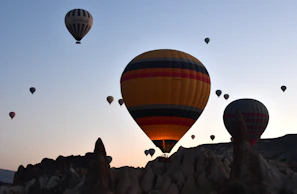 A fleet of grand balloons soaring in formation beneath a warm sunrise, with silhouettes of palm trees below.