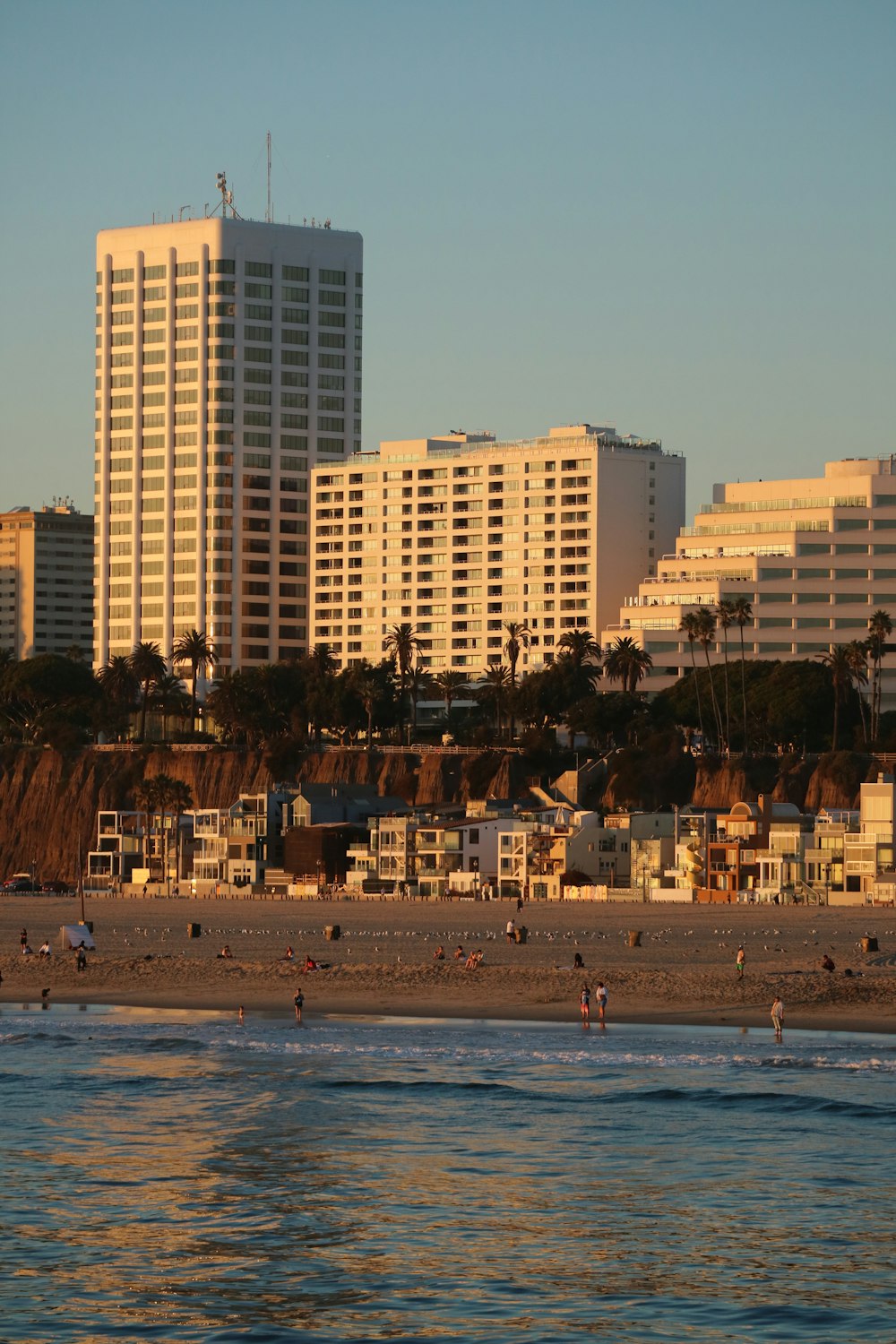 a group of people walking along a beach next to tall buildings