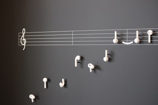 A creative arrangement of white earphones mimicking musical notes on a blackboard, with a treble clef and staff lines providing a musical context.