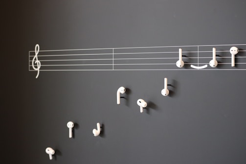 A creative arrangement of white earphones mimicking musical notes on a blackboard, with a treble clef and staff lines providing a musical context.