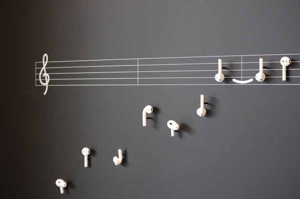 A creative arrangement of white earphones mimicking musical notes on a blackboard, with a treble clef and staff lines providing a musical context.