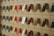 A wooden wall displays an organized array of phone cases in various colors, arranged on square panels. Each case is mounted vertically, showcasing a spectrum of hues including green, orange, pink, and blue. A small sign labeled 'Self-Checkout Available' is positioned among the cases.