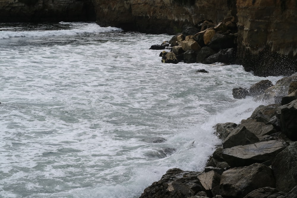 a man standing on top of a rocky beach next to the ocean