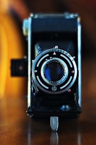 A close-up of a vintage camera resting on a wooden table with blurred background.
