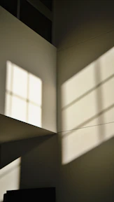 Close-up of unique geometric window casting soft natural light onto creamy white walls.