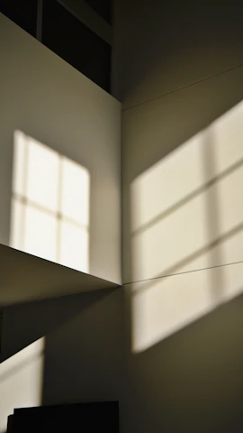 Close-up of unique geometric window casting soft natural light onto creamy white walls.