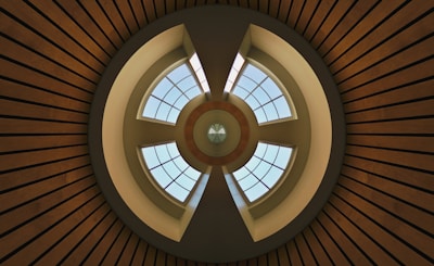 A symmetrical architectural design with concentric circles and intersecting lines, featuring a circular skylight with grid-patterned windows that allow natural light to enter. The structure exhibits a combination of geometric shapes and clean lines, with wooden slats radiating outward.