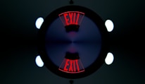 A symmetrical, kaleidoscope-like image featuring the word 'EXIT' in bold red letters repeated twice. The letters are displayed at opposite ends, surrounded by a dark circle with a gradient of blue and purple at the center. Bright circular lights appear at the four corners of the image, contributing to the geometric and symmetrical design.