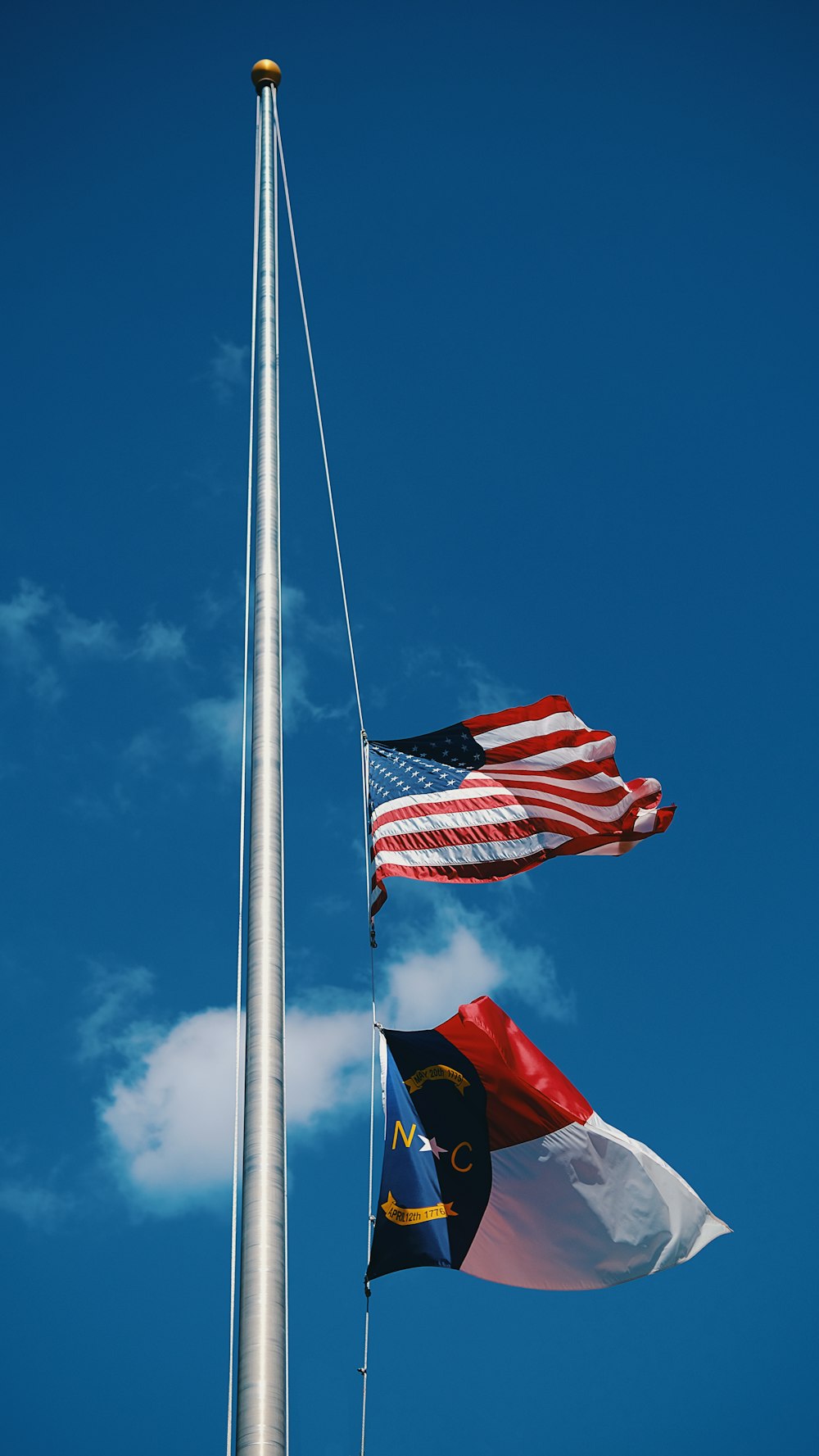 three flags flying in the wind next to a flag pole