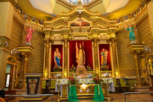 A beautifully decorated church altar with maroon and gold floral arrangements glowing under soft candlelight.
