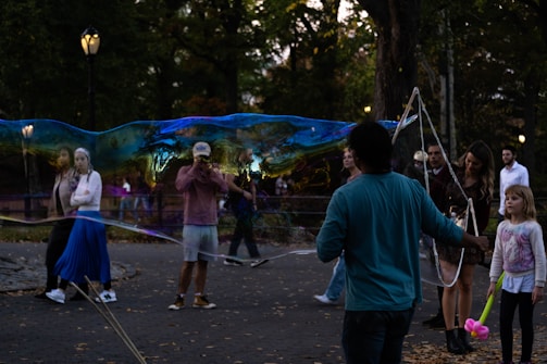 A whimsical clown entertainer making balloon animals for a group of laughing kids at a sunny park event.