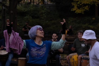 A diverse group of people sitting in a circle outdoors, joyfully playing drums together under warm sunlight.