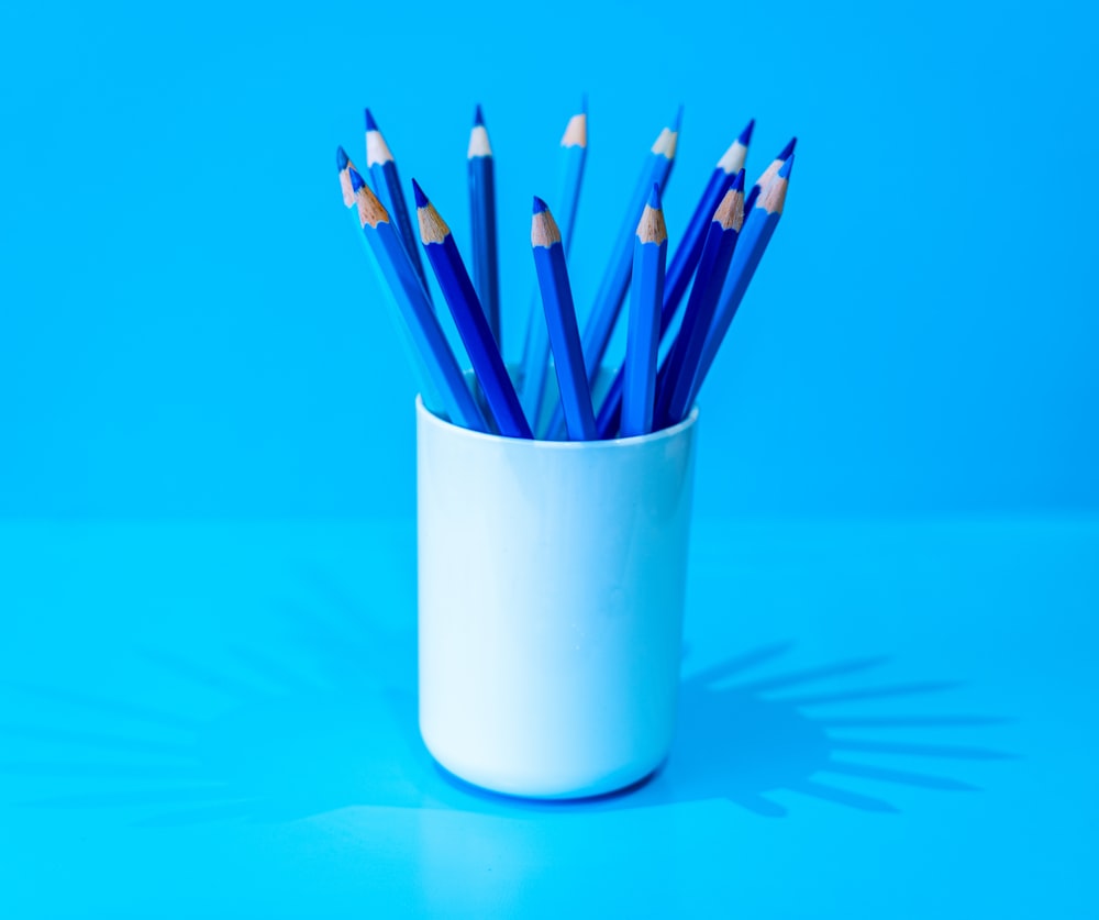 a white cup filled with blue and yellow pencils