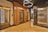 An elegant elevator lobby with three elevators, two with ornate wood paneling and one with a modern metallic finish. A stylish light fixture with circular designs hangs overhead, and the floor is covered with polished wooden planks.