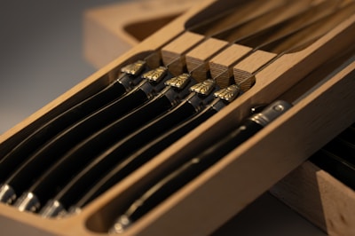 A box containing multiple neatly arranged knives with wooden handles and metallic detailing, housed in a wooden tray.