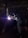 A person wearing a welding helmet is working on a metal structure with a bright welding torch. The surroundings are dark, with industrial equipment and a corrugated metal wall visible in the background.