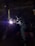 A person wearing a welding helmet is working on a metal structure with a bright welding torch. The surroundings are dark, with industrial equipment and a corrugated metal wall visible in the background.