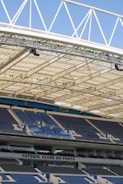Rows of blue and gray seats in a modern football stadium are positioned under a large, white, lattice-style roof structure. The seating area features the name 'FUTEBOL CLUBE DO PORTO' prominently displayed.