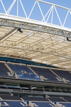 Rows of blue and gray seats in a modern football stadium are positioned under a large, white, lattice-style roof structure. The seating area features the name 'FUTEBOL CLUBE DO PORTO' prominently displayed.