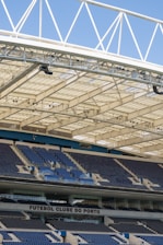 Rows of blue and gray seats in a modern football stadium are positioned under a large, white, lattice-style roof structure. The seating area features the name 'FUTEBOL CLUBE DO PORTO' prominently displayed.