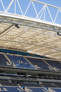 Rows of blue and gray seats in a modern football stadium are positioned under a large, white, lattice-style roof structure. The seating area features the name 'FUTEBOL CLUBE DO PORTO' prominently displayed.