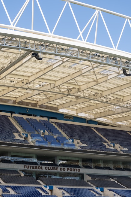 Rows of blue and gray seats in a modern football stadium are positioned under a large, white, lattice-style roof structure. The seating area features the name 'FUTEBOL CLUBE DO PORTO' prominently displayed.