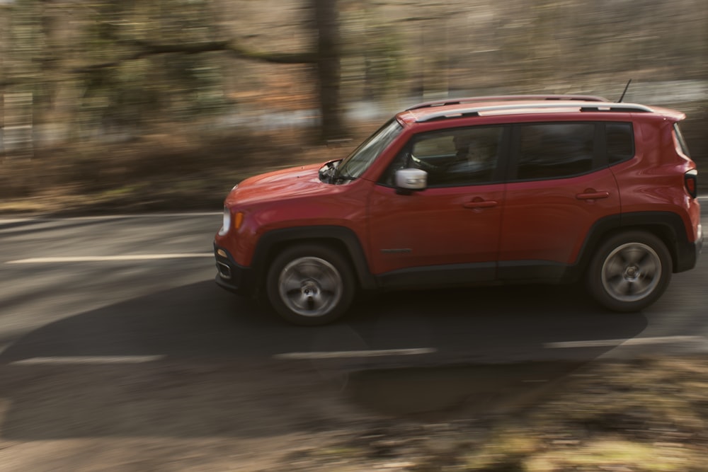 a red jeep driving down a road next to a forest