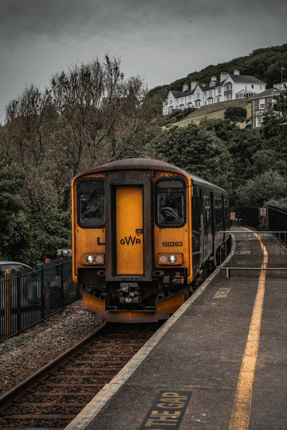 a yellow train traveling down train tracks next to a lush green hillside