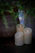 A softly lit candle resting on a black marble surface with a touch of green foliage and a hint of gold accents.