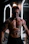A muscular person with fake severe injuries and makeup giving a gory appearance, standing in front of illuminated mirrors in a dimly lit room. The individual has an aggressive facial expression and is covered in realistic body paint depicting cuts and bruises.