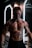 A muscular person with fake severe injuries and makeup giving a gory appearance, standing in front of illuminated mirrors in a dimly lit room. The individual has an aggressive facial expression and is covered in realistic body paint depicting cuts and bruises.