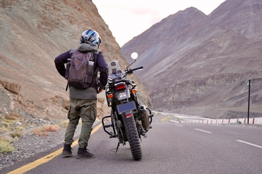 A candid shot of Alfaisal on a winding mountain road, motorcycling with a helmet and gear, the rugged landscape stretching behind.