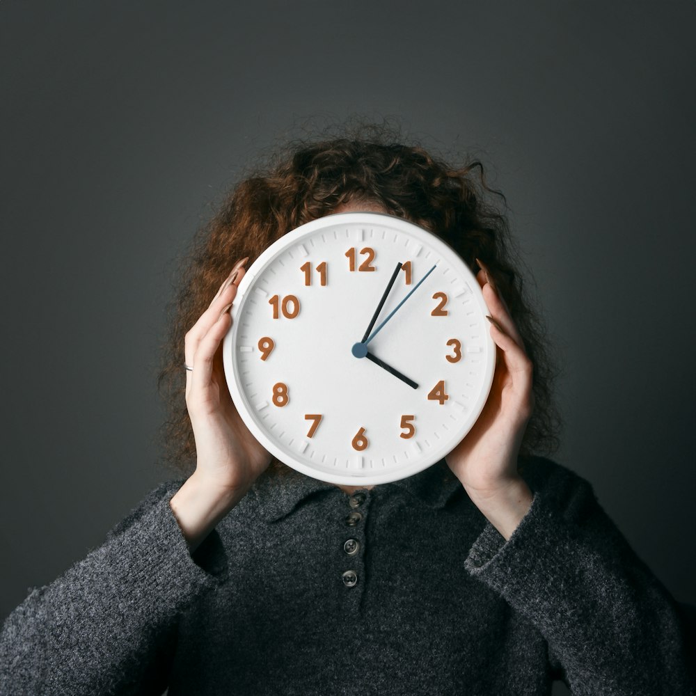 a woman covering her face with a clock