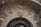 An intricately carved stone facade features an ornate face with flowing hair and a majestic expression. Surrounding the face are elaborate scrolls and leaf designs, adding a sense of grandeur to the architecture. A security camera is mounted on the top left corner.
