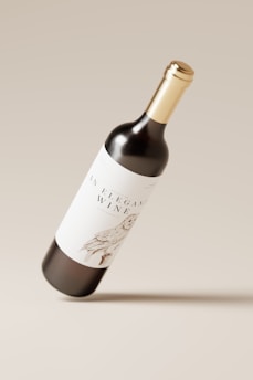 A wine bottle with a gold cap is hovering against a neutral beige background. The label features elegant typography and a detailed illustration of a bird.