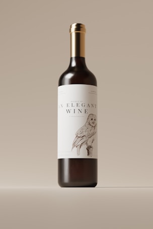 A wine bottle with a sleek and elegant design is centered against a neutral background. The label features an illustration of an owl, adding a touch of artistic charm, and prominently displays the text 'An Elegant Wine.' The bottle has a dark body with a shiny metallic gold cap.